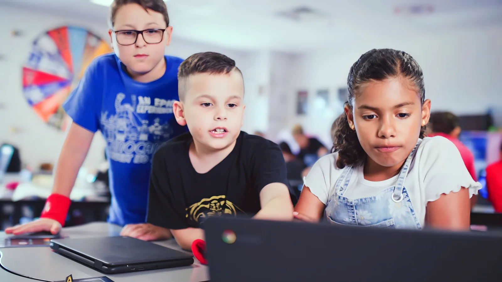 Three students gathered around a laptop, working through a task together